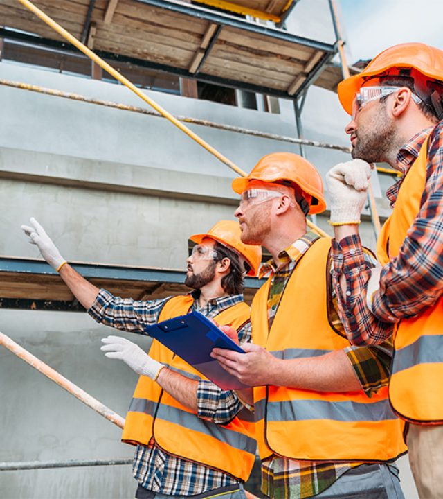 group of builders in hard hats and reflective vests pointing at building house