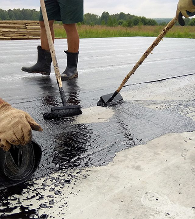 Roofer worker painting bitumen praimer at concrete surface by the roller brush Waterproofing 2018